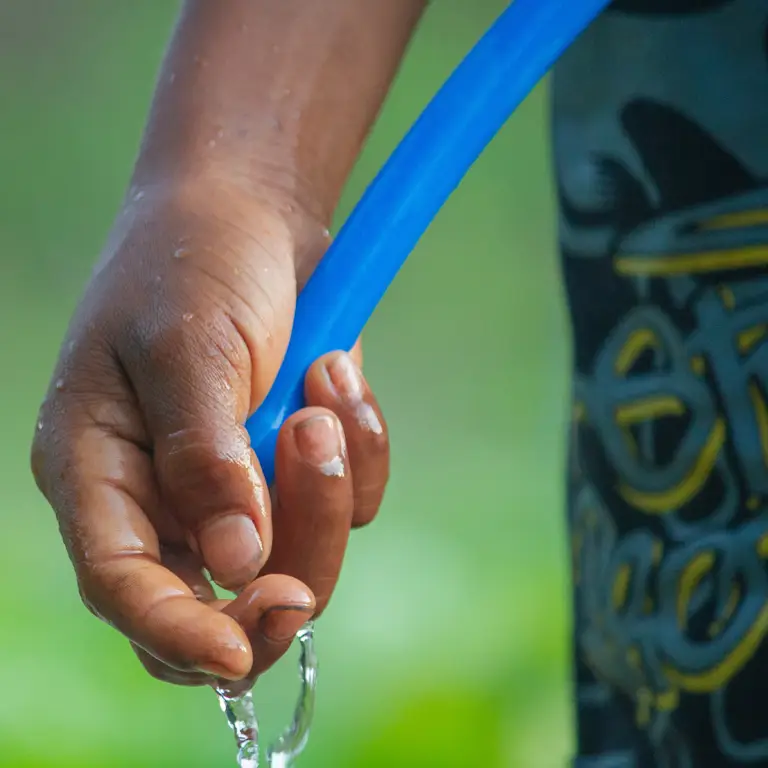 Main tenant un tuyau d'arrosage, l'eau s'écoulant sur un sol sec en août pour illustrer l'évaporation