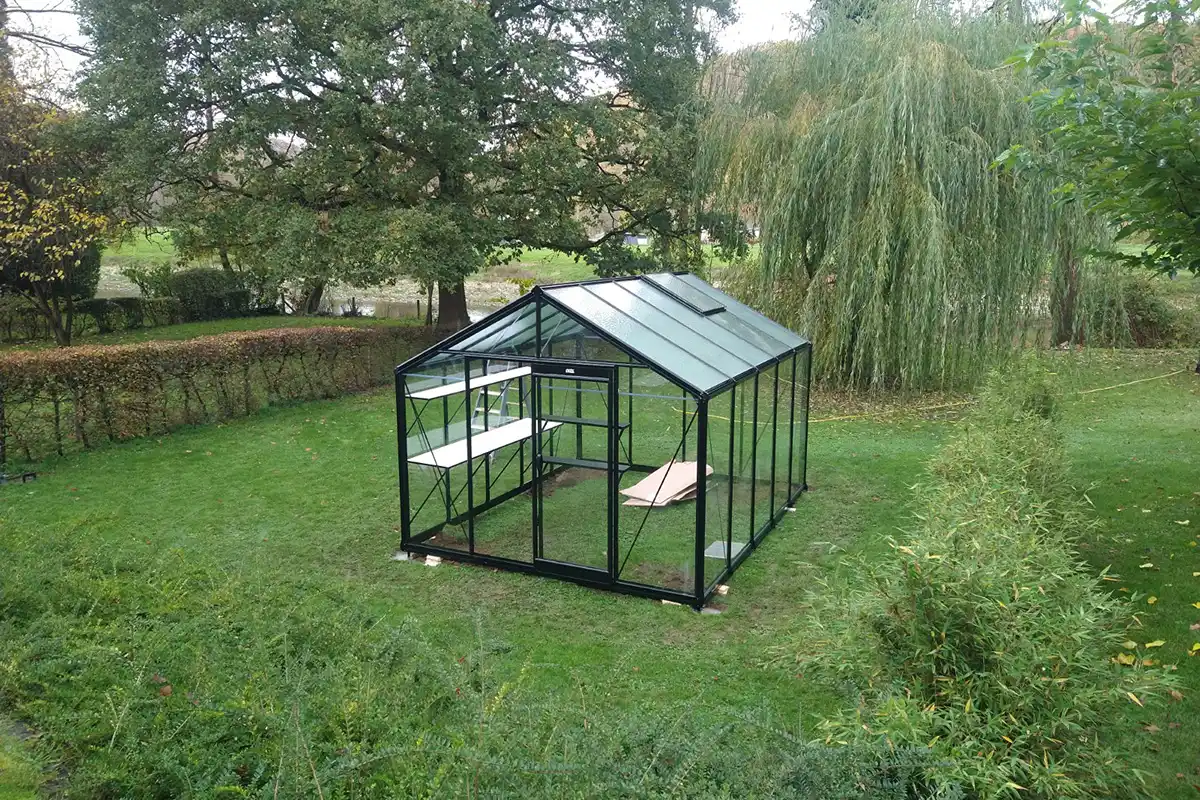 Dans un jardin, une serre en verre qui vient d'être installée
